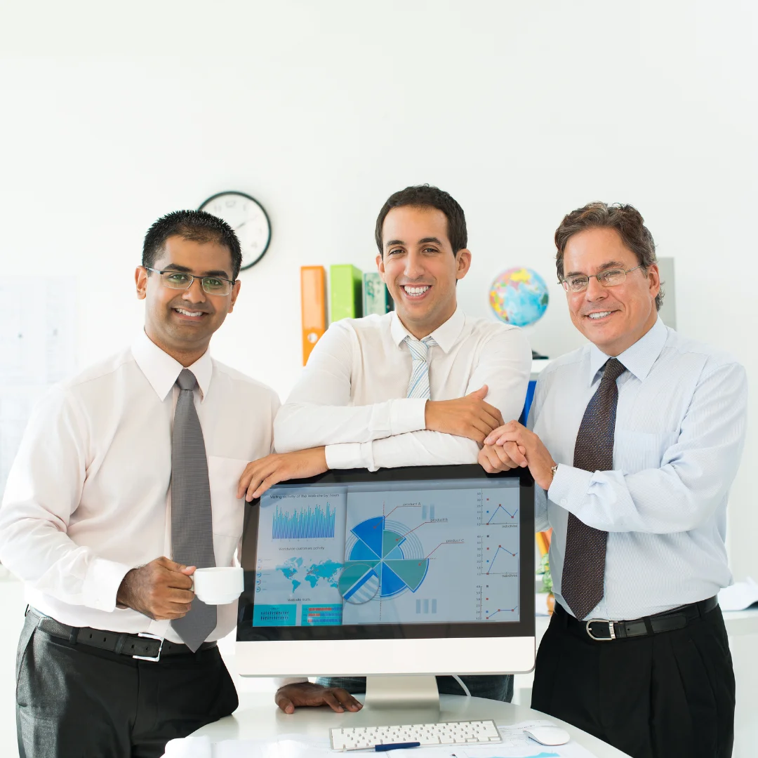 Three men standing together in front of a computer, engaged in discussion or collaboration.
