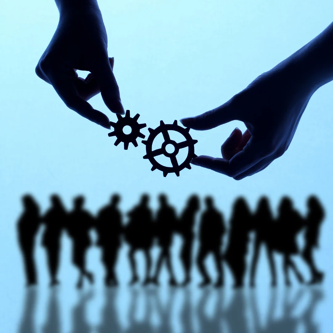 Silhouette of people holding gears, surrounded by a diverse group of individuals, symbolizing teamwork and collaboration.
